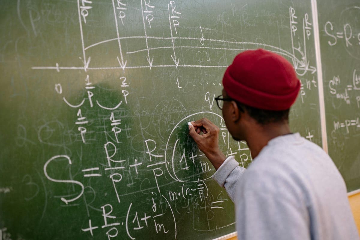 A student writing equations on a blackboard covered in formulas