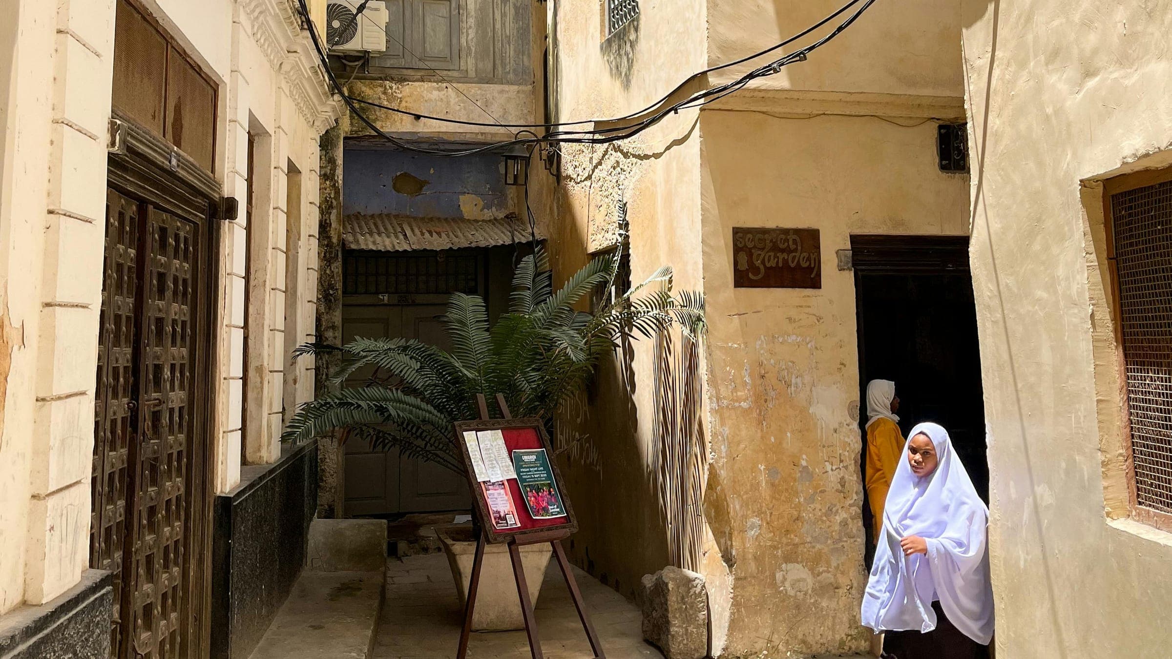A woman in a white headscarf in a narrow alley of old stone buildings in Stone Town, Zanzibar