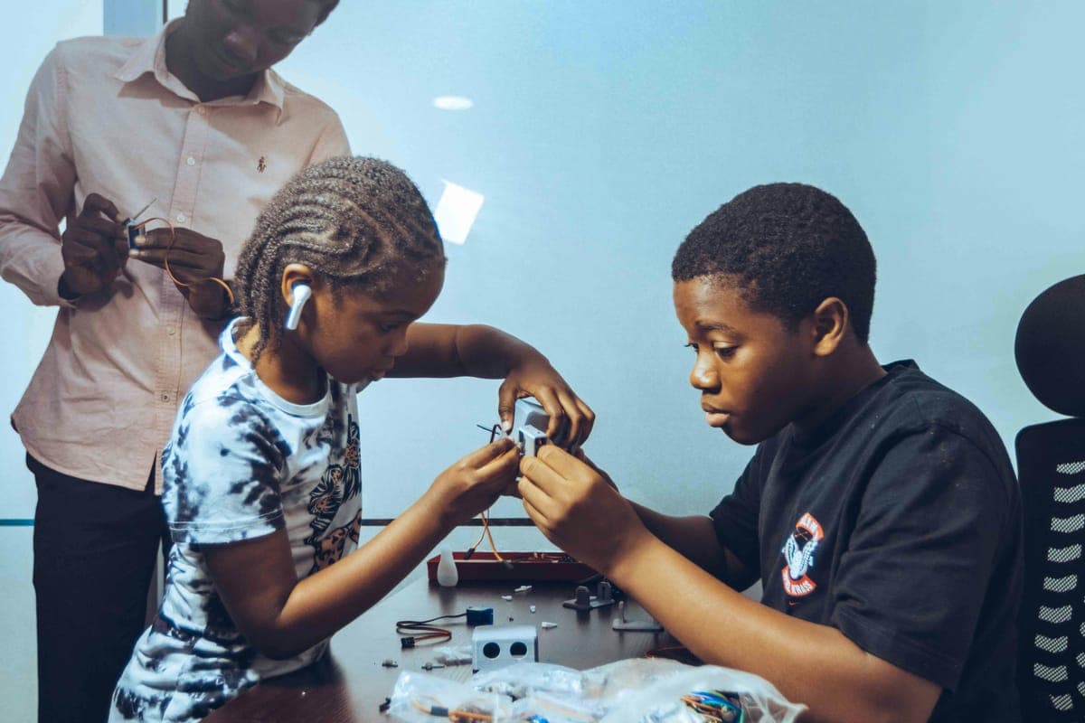Two students wiring an electronics kit together while a mentor looks on