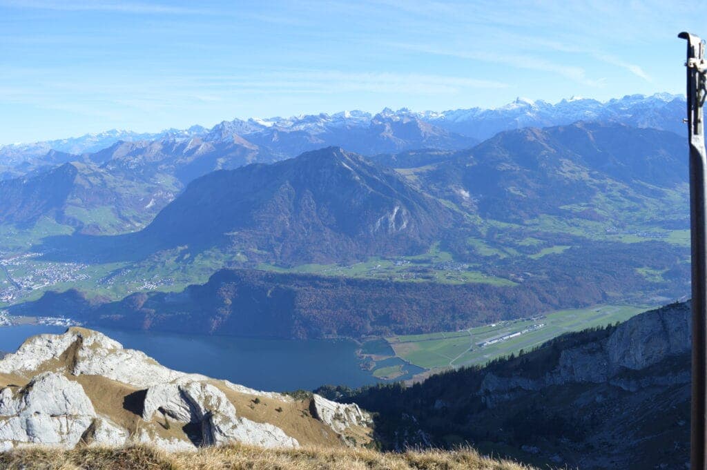 The view from a mountain summit over a lake and the snow-capped Alps