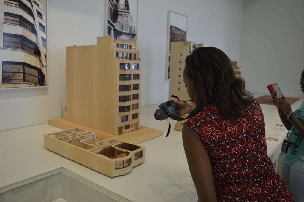 A student photographing an architectural model of an apartment building in a gallery